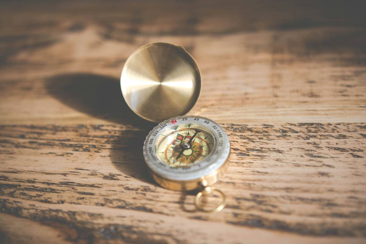 Three types of classic home compasses: brass marine compass, wooden baseplate compass, and antique pocket compass mounted on a shelf with feng shui elements